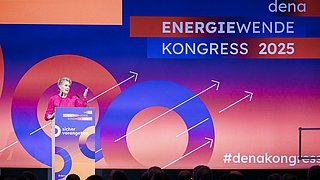 Corinna Enders, Vorsitzende der dena-Geschäftsführung, steht am Rednerpult auf dem dena Energiewende-Kongress 2025 vor einer großen Leinwand mit dem Schriftzug 'ENERGIEWENDE KONGRESS 2025' und mehreren weißen Pfeilen nach oben.