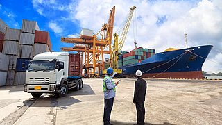 Zwei Männer stehen in der Nähe eines Lastwagens und eines Containerschiffs.