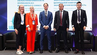 Fünf Personen stehen nebeneinander auf einer Bühne vor einer Leinwand mit dem Titel „Energietransformation in Zentralasien als wirtschaftliche Chance“. Von links nach rechts: Kim Lakeit (Leiterin Stabsstelle Internationale Kooperationen der dena), Ekaterina Galitsyna (Leiterin der Abteilung für Osteuropa, Zentralasien und den Südkaukasus, KfW IPEX-Bank), Dr. Urs Engels (Leiter des Referats für Zentralasien, BMWK), Sungat Yessimkhanov (Vizeminister für Energie der Republik Kasachstan) und Maxim Zubov (Generaldirektor Siemens Energy Kasachstan, Vizepräsident für die Subregionen Türkei, Südkaukasus und Zentralasien). Alle tragen formelle Businesskleidung und stehen lächelnd vor einer Konferenzbühne mit Sesseln und Mikrofonen