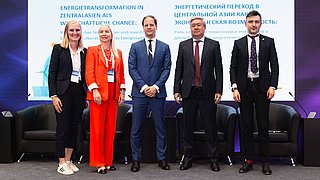 Fünf Personen stehen nebeneinander auf einer Bühne vor einer Leinwand mit dem Titel „Energietransformation in Zentralasien als wirtschaftliche Chance“. Von links nach rechts: Kim Lakeit (Leiterin Stabsstelle Internationale Kooperationen der dena), Ekaterina Galitsyna (Leiterin der Abteilung für Osteuropa, Zentralasien und den Südkaukasus, KfW IPEX-Bank), Dr. Urs Engels (Leiter des Referats für Zentralasien, BMWK), Sungat Yessimkhanov (Vizeminister für Energie der Republik Kasachstan) und Maxim Zubov (Generaldirektor Siemens Energy Kasachstan, Vizepräsident für die Subregionen Türkei, Südkaukasus und Zentralasien). Alle tragen formelle Businesskleidung und stehen lächelnd vor einer Konferenzbühne mit Sesseln und Mikrofonen