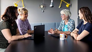 Vier Frauen sitzen an einem Tisch und sprechen miteinander.