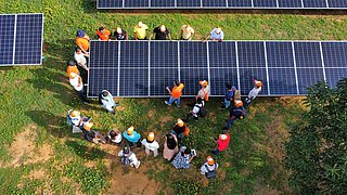 Dieses Bild zeigt eine größere Gruppe von Menschen, die in einem Solarpark von oben zu sehen sind.