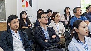 Mehrere Teilnehmende der Veranstaltung sitzen auf Stühlen in Reihen und hören zu.