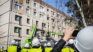 Zuschauerinnen und Zuschauer schauen bei der Montage von vorgefertigten Fassadenteilen zu.