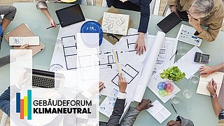 Ein Tisch mit mehreren Personen, die an Plänen und Skizzen arbeiten. Sichtbare Materialien sind Notizblätter, ein Laptop und ein Pflanzenarrangement. Links unten das Logo 'GEBÄUDEFORUM KLIMANEUTRAL'.