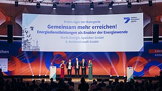 Fünf Personen stehen auf einer Bühne bei einer Preisverleihung des Energy Efficiency Award, vor einer großen Leinwand mit dem Text „Preisträger der Kategorie Gemeinsam mehr erreichen! Energiedienstleistungen als Enabler der Energiewende Stadt.Energie.Speicher GmbH& denkmalstadt GmbH“