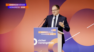 Carsten Schneider, Bundesminister für Umwelt, Klimaschutz, Naturschutz und nukleare Sicherheit,  in dunklem Anzug und Krawatte steht hinter einem Rednerpult mit dem Schriftzug 'sicher vorangehen' beim dena Energiewende-Kongress 2025
