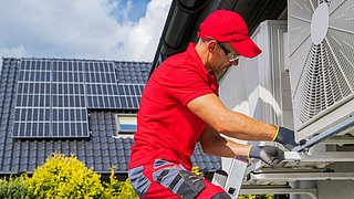 Ein Handwerker montiert eine Klimaanlage an einer Hauswand.