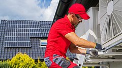 Ein Handwerker montiert eine Klimaanlage an einer Hauswand.