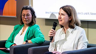 Im Vordergrund leistet Sara Bäumchen einen Diskussionsbeitrag, im Hintergrund sitzt Michaela Steinhauser auf dem Podium.
