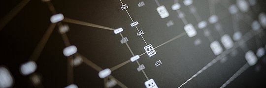 Visualisierung eines komplexen digitalen Netzwerks mit verbundenen Symbolen und Knotenpunkten auf einem dunklen Hintergrund, die auf eine Datenstruktur oder Prozessarchitektur hinweisen.