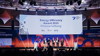 Fünf Personen auf Bühne bei der Preisverleihung des Energy Efficiency Award 2025, großes Banner mit Text und Logos von dena und KfW im Hintergrund.