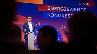 Mann im blauen Anzug steht am Rednerpult vor einer Wand mit Schriftzug 'ENERGIEWENDE KONGRESS' und 'dena'.
