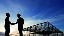 Zwei Bauarbeiter schütteln sich die Hand vor einem Rohbau im Sonnenuntergang