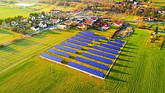 Luftaufnahme eines Solarparks in der ländlichen Umgebung, mit zahlreichen Solarpanelen, die in der Sonne glänzen.