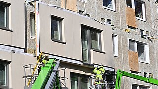 Arbeiter in Hebebühnen montieren neue Fassadenplatten an einem Wohngebäude.