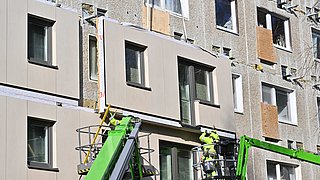 Arbeiter in Hebebühnen montieren neue Fassadenplatten an einem Wohngebäude.
