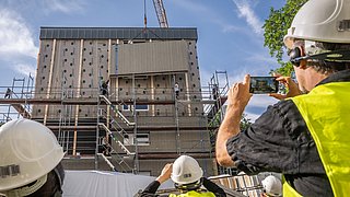 Bauarbeiter mit Helm und gelber Warnweste vor einem Gebäude, das seriell saniert wird