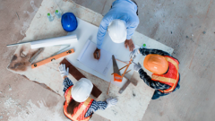 drei Personen, die an einem Tisch stehen und Bauarbeiter-Helme tragen