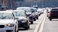 Stau mit mehreren Autos auf einer Straße. Sichtbare Fahrzeuge sind in verschiedenen Farben, darunter Weiß, Schwarz und Silber.