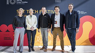 Fünf Personen stehen vor einer farbigen Wand mit dem Schriftzug 'SET TECH FESTIVAL' und Logos von 'Start Up Energy Transition' und 'dena'