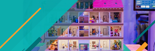 Im Hintergrund ist der physi-sche Gebäudedemonstrator DEEP zu sehen. Im Vorder-grund befinden sich, jeweils seitlich, farbige Balken.