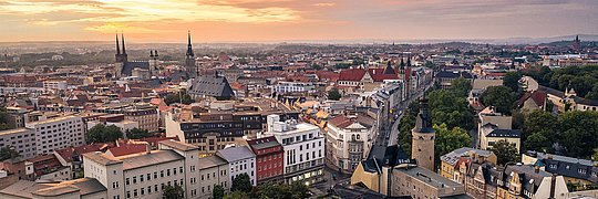 Stadtpanorama von Halle (Saale) bei Sonnenuntergang mit historischen Gebäuden, Kirchtürmen und dicht bebauten Straßen.