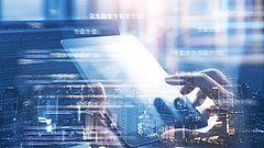 Eine Hand hält ein Tablet, während im Hintergrund verschwommene Stadtlichter und digitale Datenströme sichtbar sind.