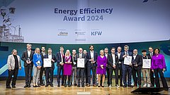 Gruppe von 17 Personen auf einer Bühne, die Auszeichnungen beim Energy Efficiency Award 2024 halten. Banner im Hintergrund mit 'Energy Efficiency Award 2024', Logos von dena und KfW.
