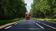 Red,Commercial,Truck,Traveling,On,Paved,Road,Through,Dense,Green