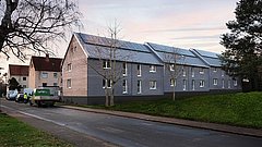 Mehrfamilienhaus mit Solarpanelen auf dem Dach in ruhiger Wohngegend.