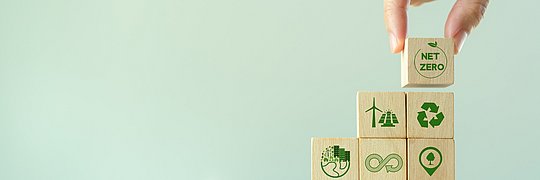Eine Hand platziert Holzwürfel übereinander auf denen Nachhaltigkeits-Symbole gedruckt sind.