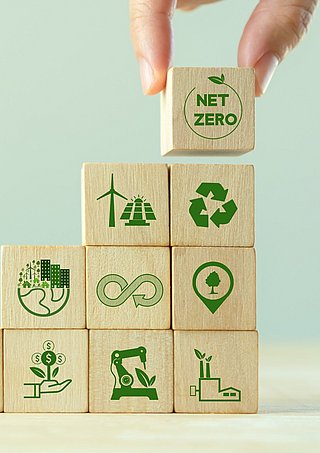 Eine Hand platziert Holzwürfel übereinander auf denen Nachhaltigkeits-Symbole gedruckt sind.