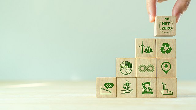 Eine Hand platziert Holzwürfel übereinander auf denen Nachhaltigkeits-Symbole gedruckt sind.