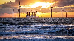 Offshore-Windpark mit Windrädern und einem Schiff bei Sonnenuntergang über dem Meer.