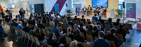 Gäste sitzen in Reihenbestuhlung vor der Bühne im Future Energy Lab
