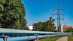 Fernwärmeleitungen mit Blockheizkraftwerk und Bäumen im Hintergrund, darüber eine Stromleitung