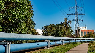 Fernwärmeleitungen mit Blockheizkraftwerk und Bäumen im Hintergrund, darüber eine Stromleitung