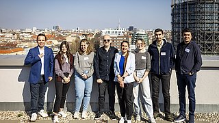 Gruppe von acht Personen steht auf einer Dachterrasse mit Stadtpanorama im Hintergrund