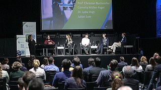 Das Bild zeigt fünf Personen auf einer Bühne auf Stühlen sitzend für eine Paneldiskussion.
