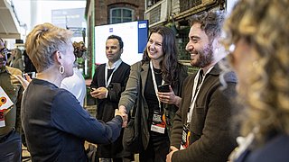 Menschen mit Namensschildern stehen in einer Halle und geben sich die Hand