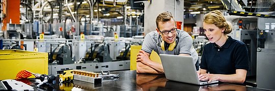 Ingenieure die in einer Werkhalle an einem Laptop arbeiten