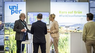 Vier Personen stehen vor einem Messestand mit den Logos 'uniper' und 'Kurs auf Grün #ForACleanTomorrow'