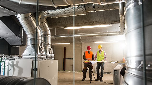 Ingenieure betrachten in einer Industriehalle Pläne