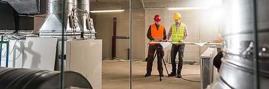 Ingenieure betrachten in einer Industriehalle Pläne