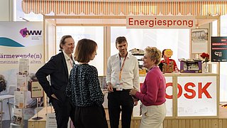 Vier Personen im Gespräch vor einem Messestand mit dem Schriftzug 'Energiesprong'