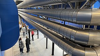 Eine Gruppe von Personen erkundet ein weitläufiges Industriegebäude mit zahlreichen Rohren.