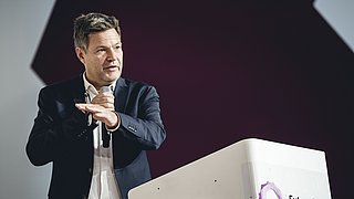 Robert Habeck in schwarzem Anzug mit Mikrofon, steht an einem weißen Rednerpult mit dem Logo 'Future Energy Lab'.