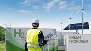Ingenieur mit Tablet-Computer vor dem Hintergrund einer grünen Wasserstofffabrik.