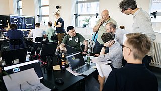 Gruppe von Teilnehmenden der EnerCise Cyberübung III in einem hellen Raum mit großen Fenstern, die an Laptops und technischen Geräten arbeiten. Die Übung kombiniert Tabletop-Elemente und Hands-on-Phasen für realistische Cybersecurity-Szenarien.